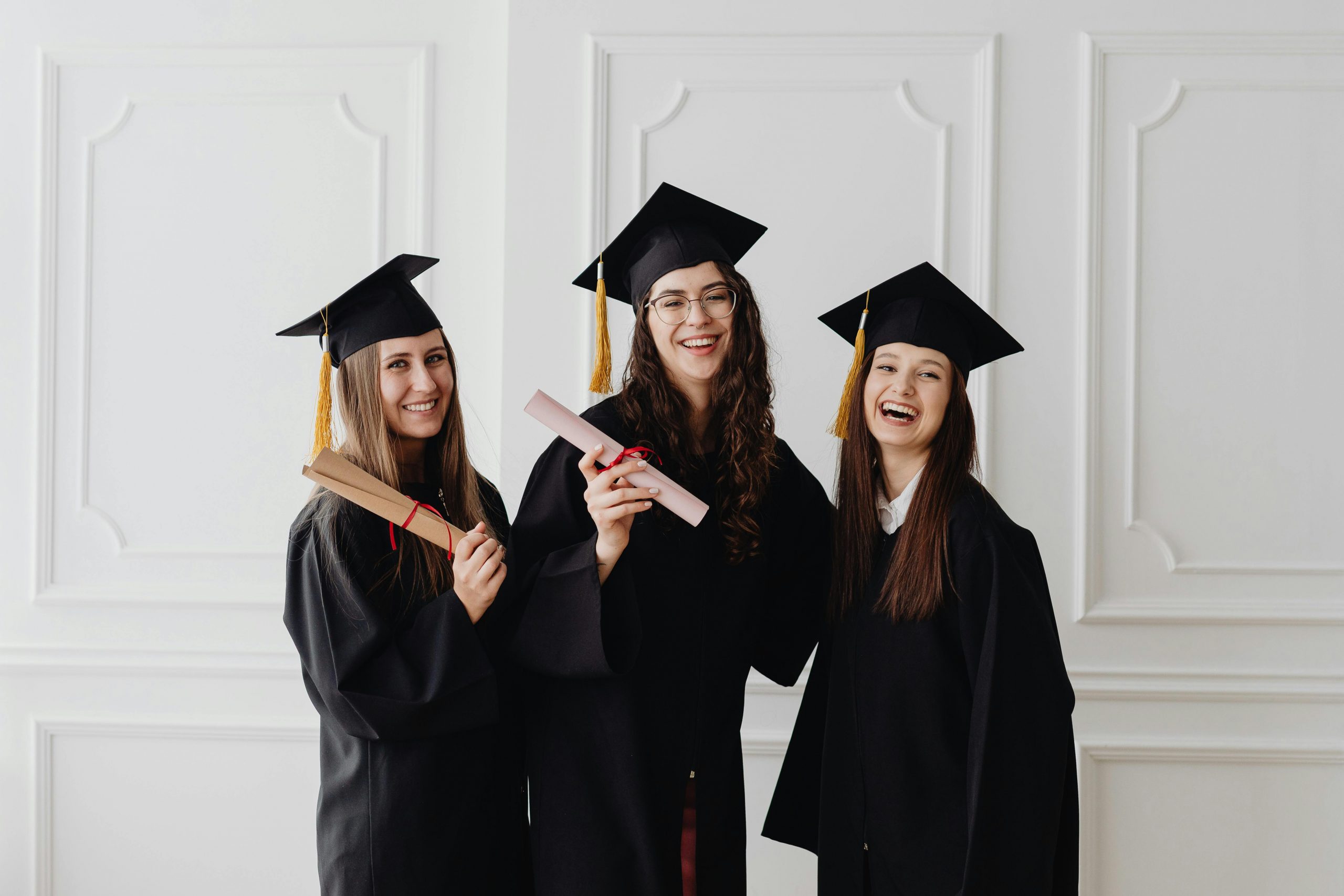 Three smiling college graduates in caps and gowns holding diplomas after commencement, representing How do Student Loans Work, Private Student Loans, managing a Student Loan Payment, learning How to Get a Student Loan, and the educational resources available through our About Us page.