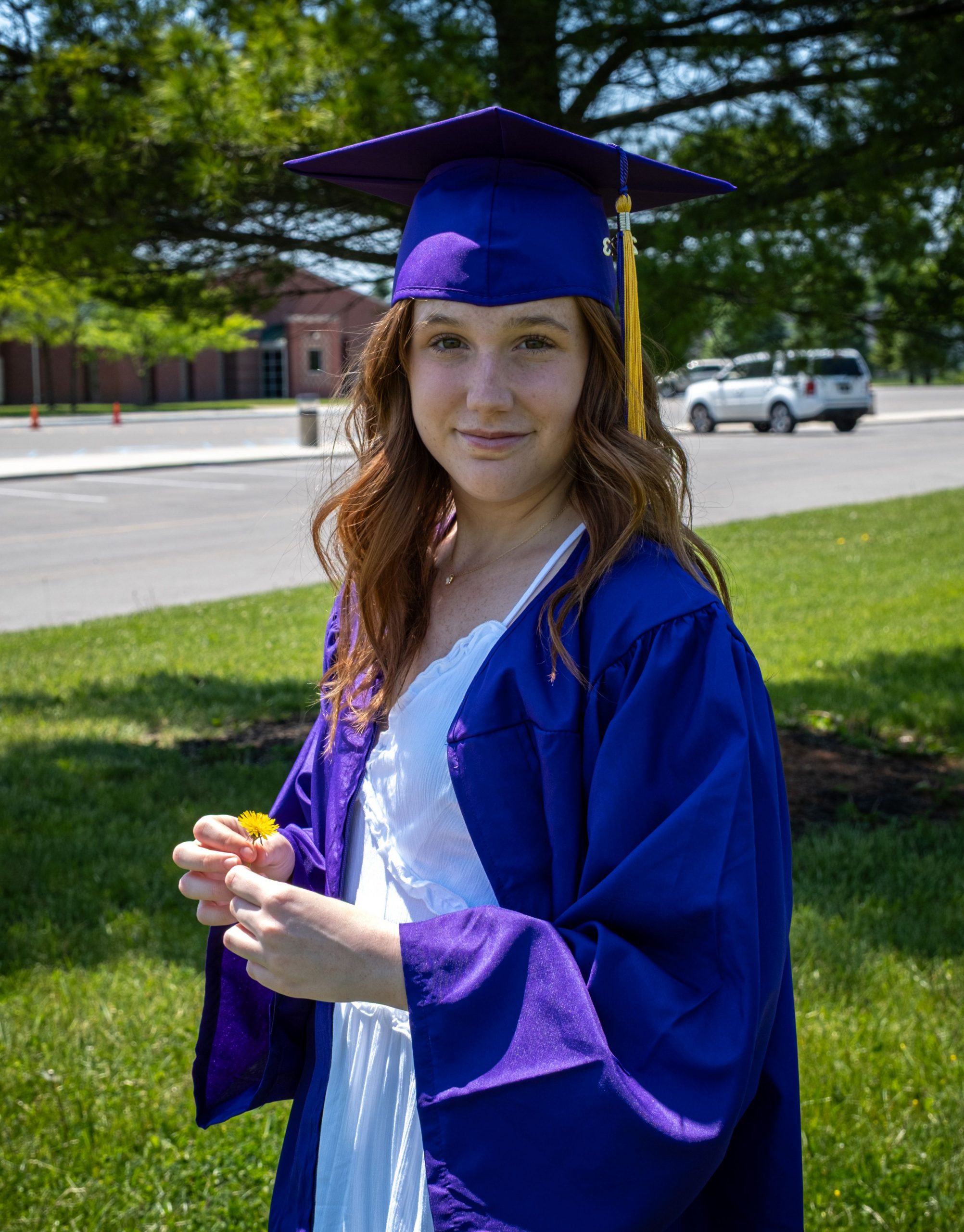Graduate standing outdoors in a blue cap and gown holding a flower, representing Student Loan Consolidation Refinance, comparing a Grad Plus Loan, researching Low Interest Student Loan Refinance options, reviewing Student Loan Refinance Rates Today, and exploring ways to Refinance Student Loans after graduation.