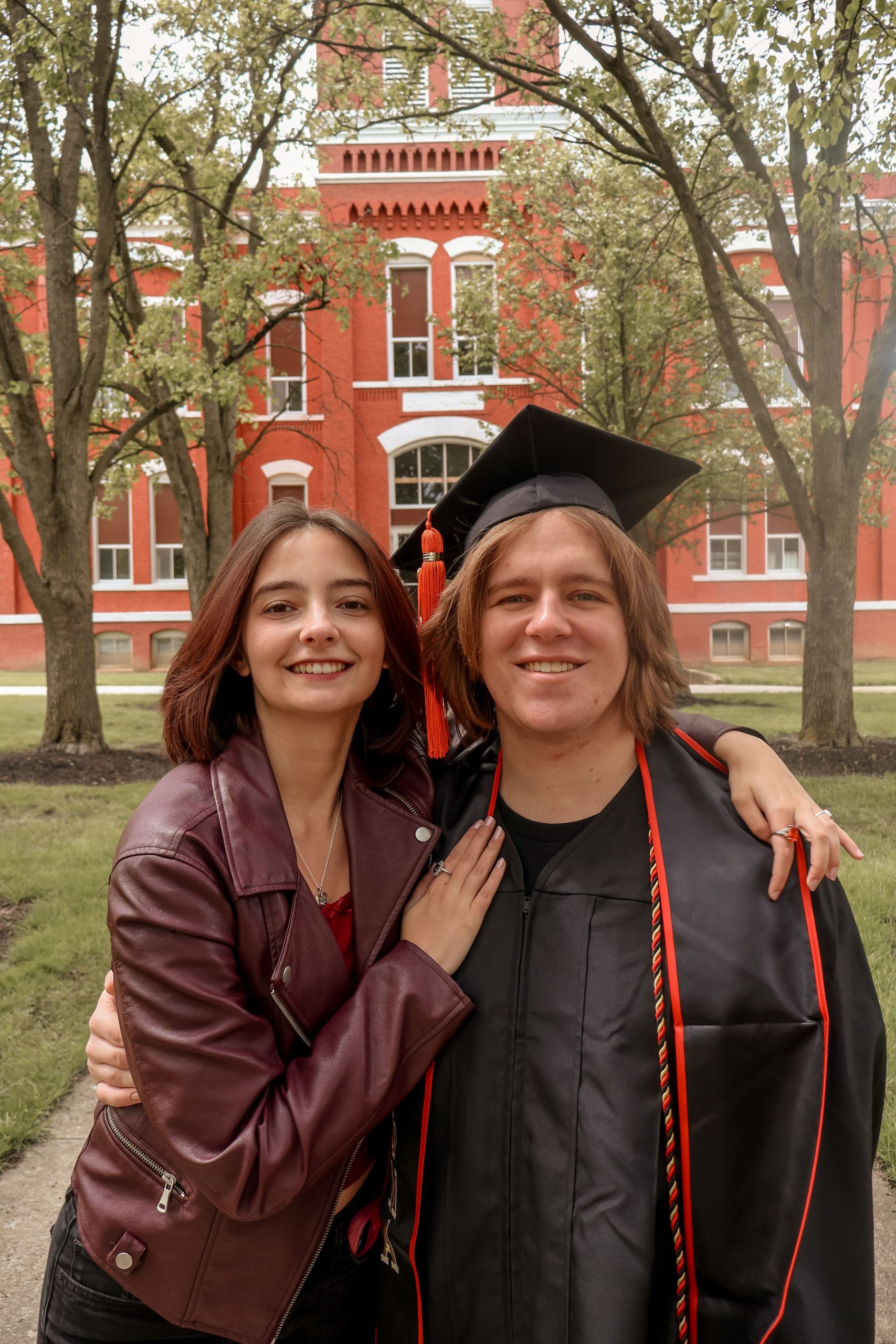 College graduate standing with a friend in front of a university building while exploring Online Student Loan Refinance options, comparing Private Student lending solutions, researching Private School Loans, reviewing the Lowest Student Loan Refinance Rates, and learning When Do Student Loans Resume after graduation or deferment.