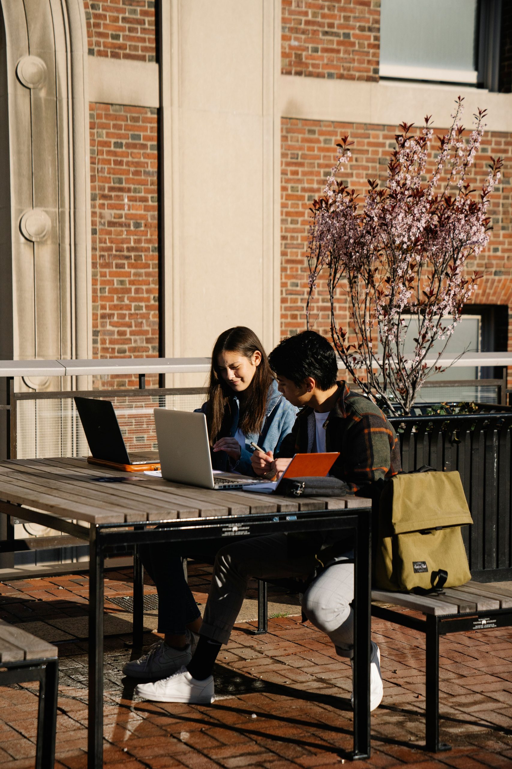 Two college students studying outdoors on campus with laptops and notebooks while researching Student Loan Refinance Companies, exploring a Public Service Loan career path, learning How often Can you Refinance Student Loans, evaluating options to Refinance International Student Loan debt, and searching for Student Loan Relief opportunities.
