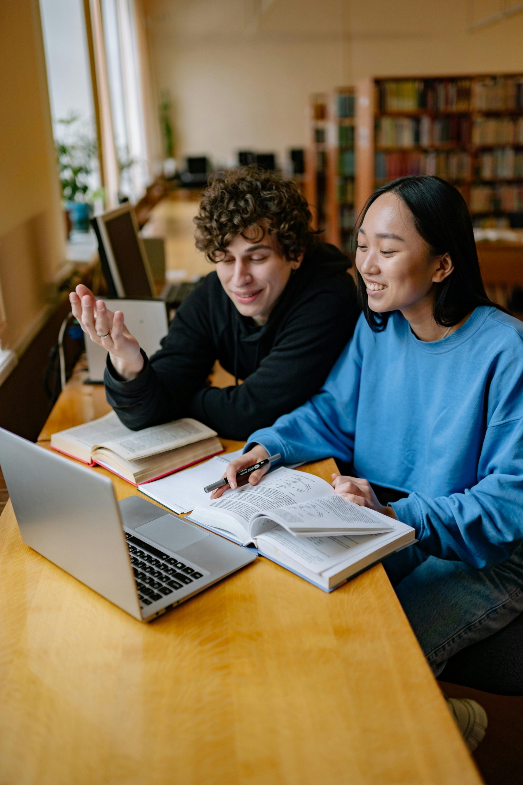 Two college students studying together on a laptop in a library while researching Student Loan Consolidation, learning the Refinance Student Loans Meaning, asking Can I Refinance My Student Loans, reviewing Federal Student Loans, and comparing options for Student Loan Repayment after graduation.